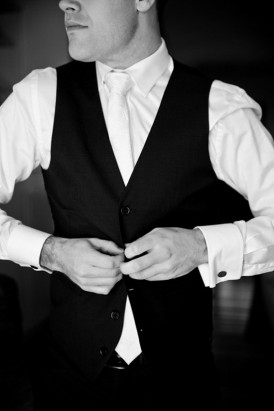 groom putting on black waistcoat